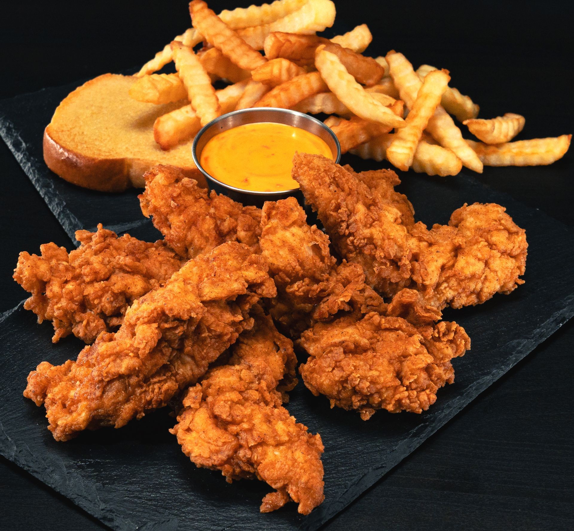 A plate of chicken fingers and french fries with a side of bread and dipping sauce.