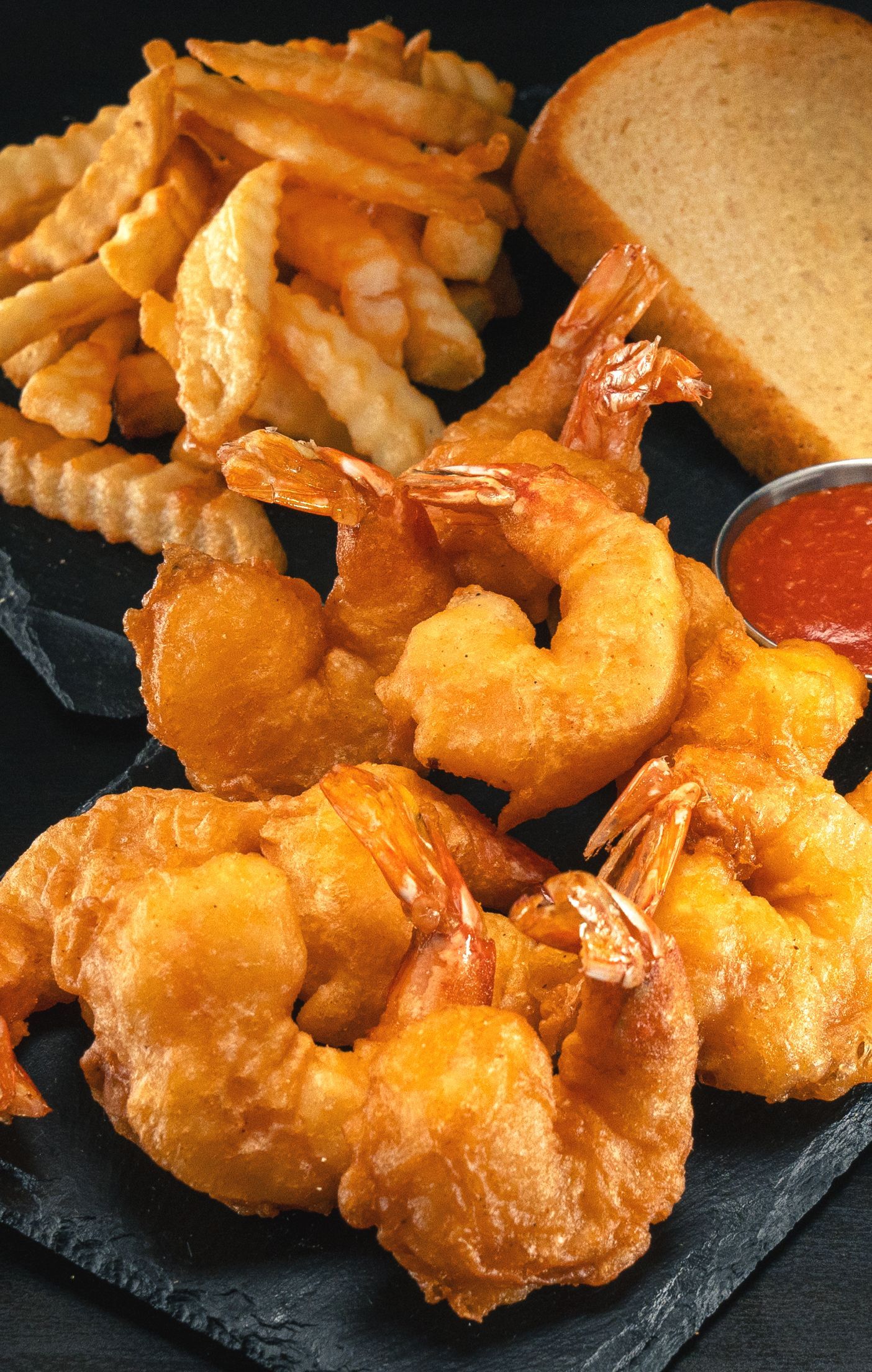 A plate of fried shrimp , french fries and a piece of bread.