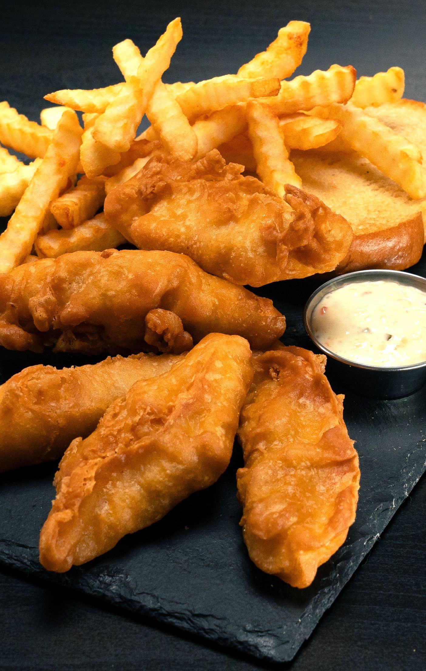 A plate of fried fish and french fries with a dipping sauce.