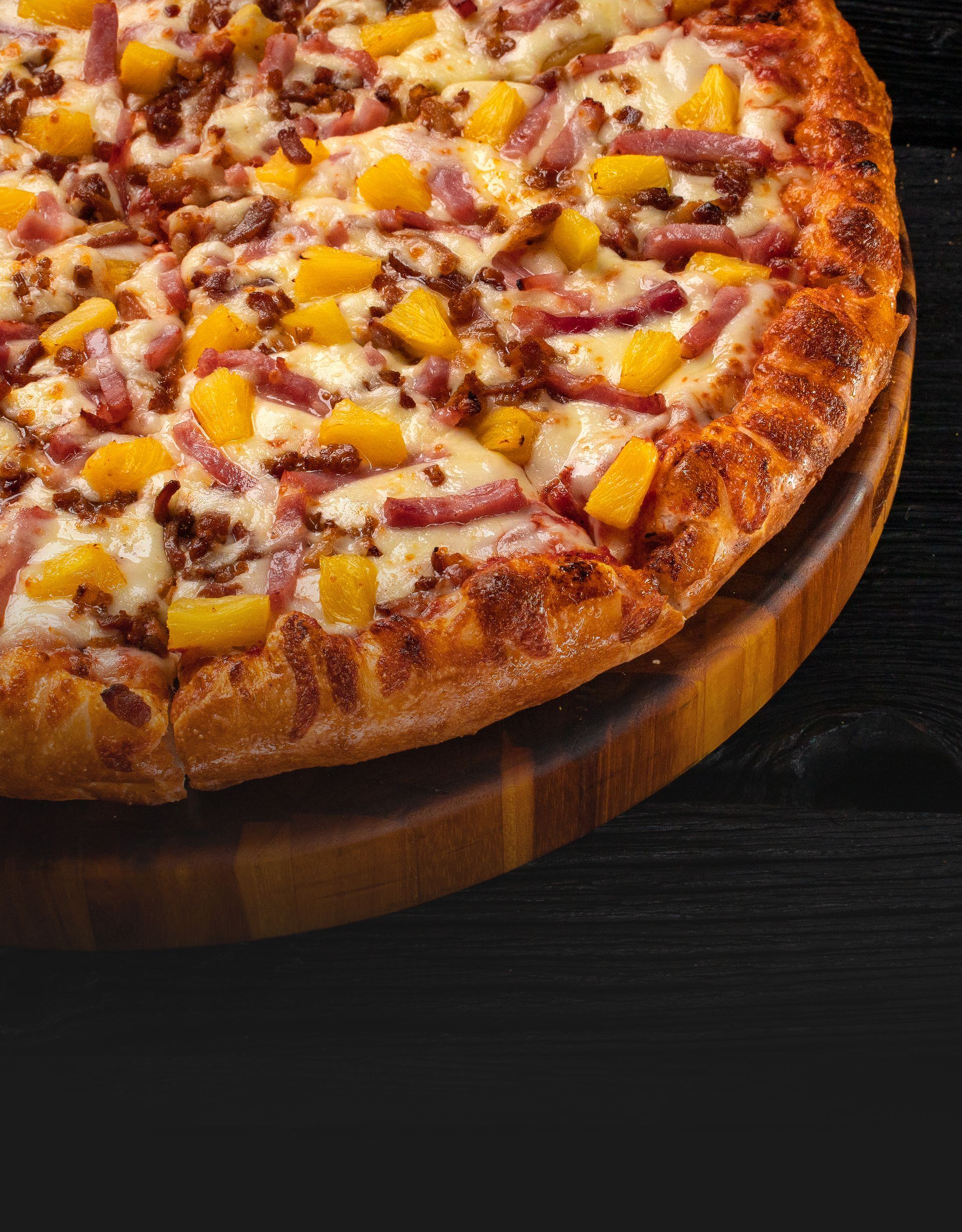 Hawaiian pizza with pineapple, bacon, and cheese on a wooden cutting board