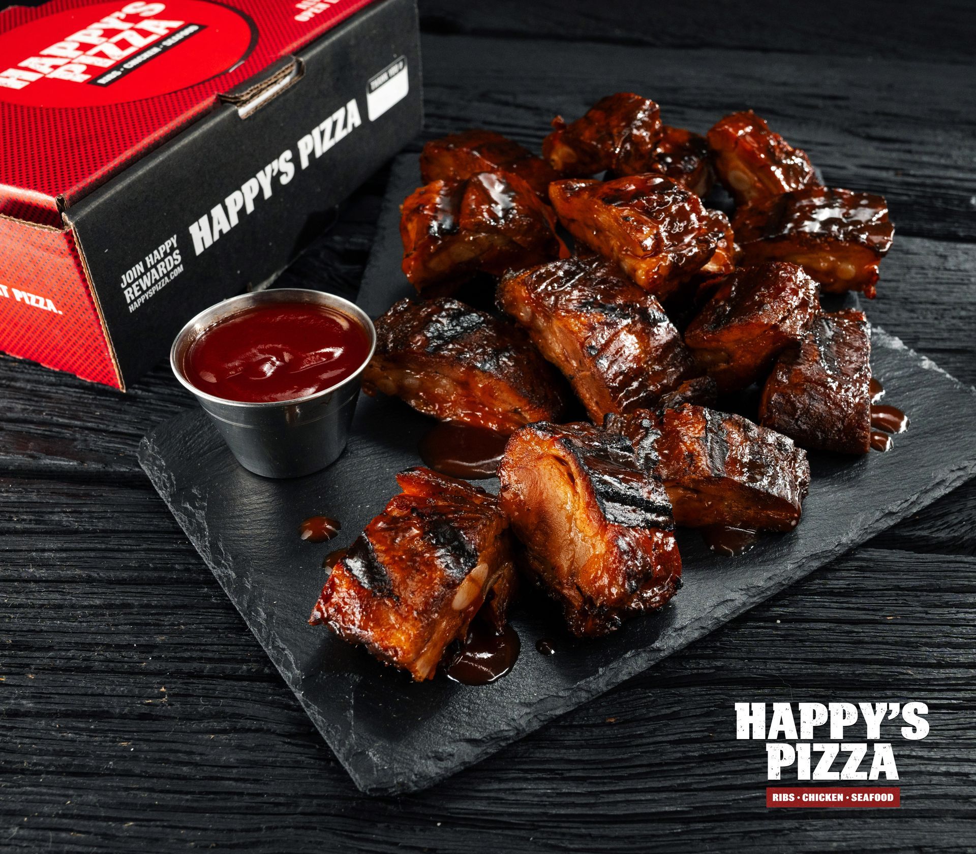 A box of happy 's pizza sits next to a plate of ribs