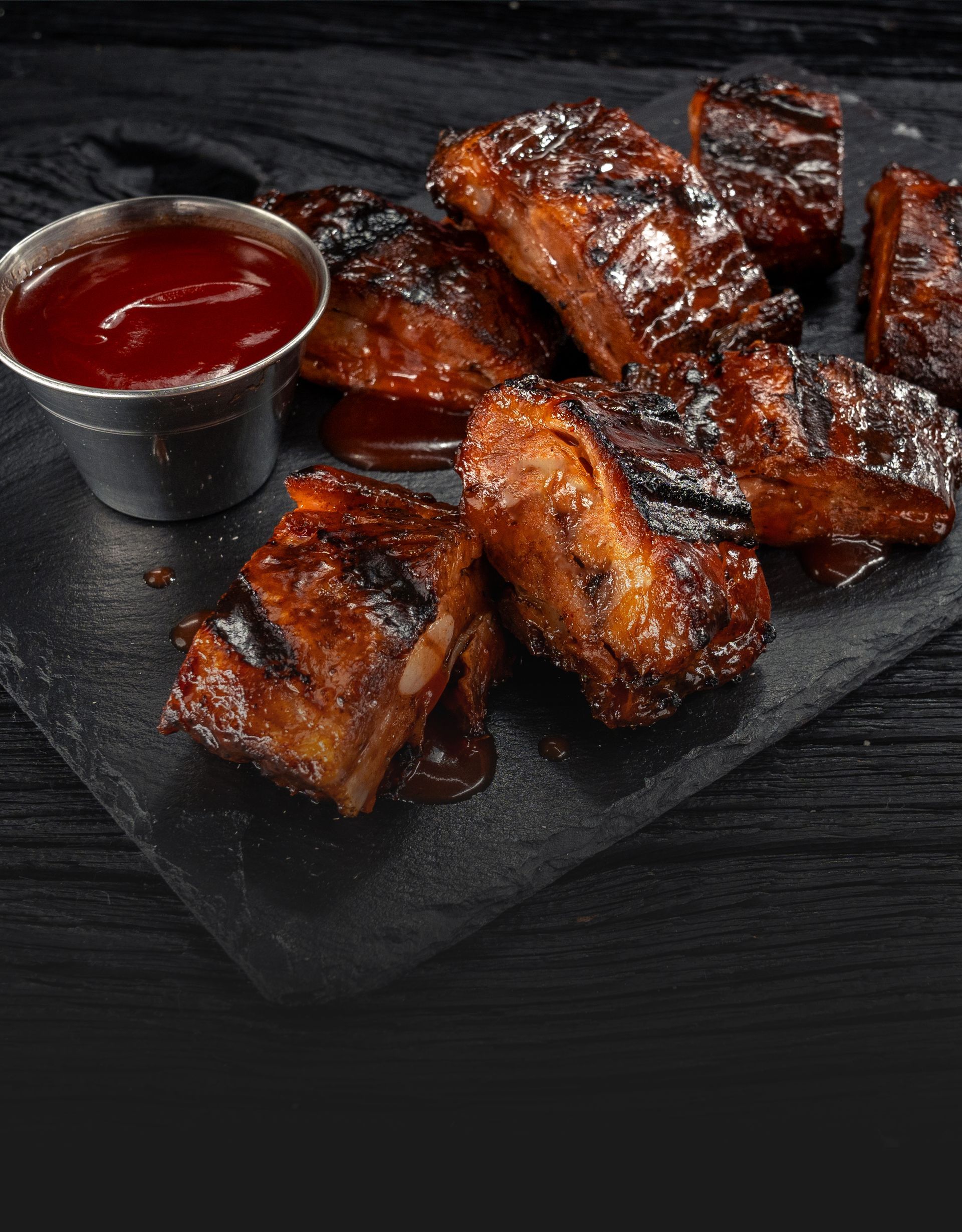 One pound of BBQ rib tips served with a side of ketchup on a black platter