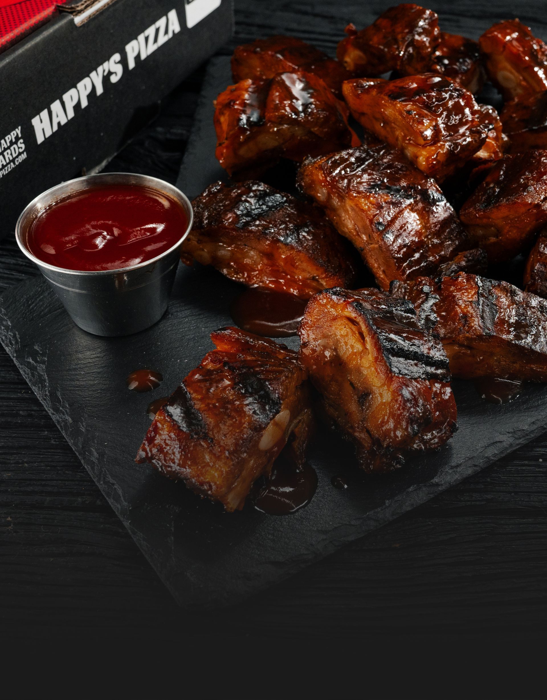 Two pounds of BBQ rib tips with a side of ketchup and a Happy's Pizza box in the background