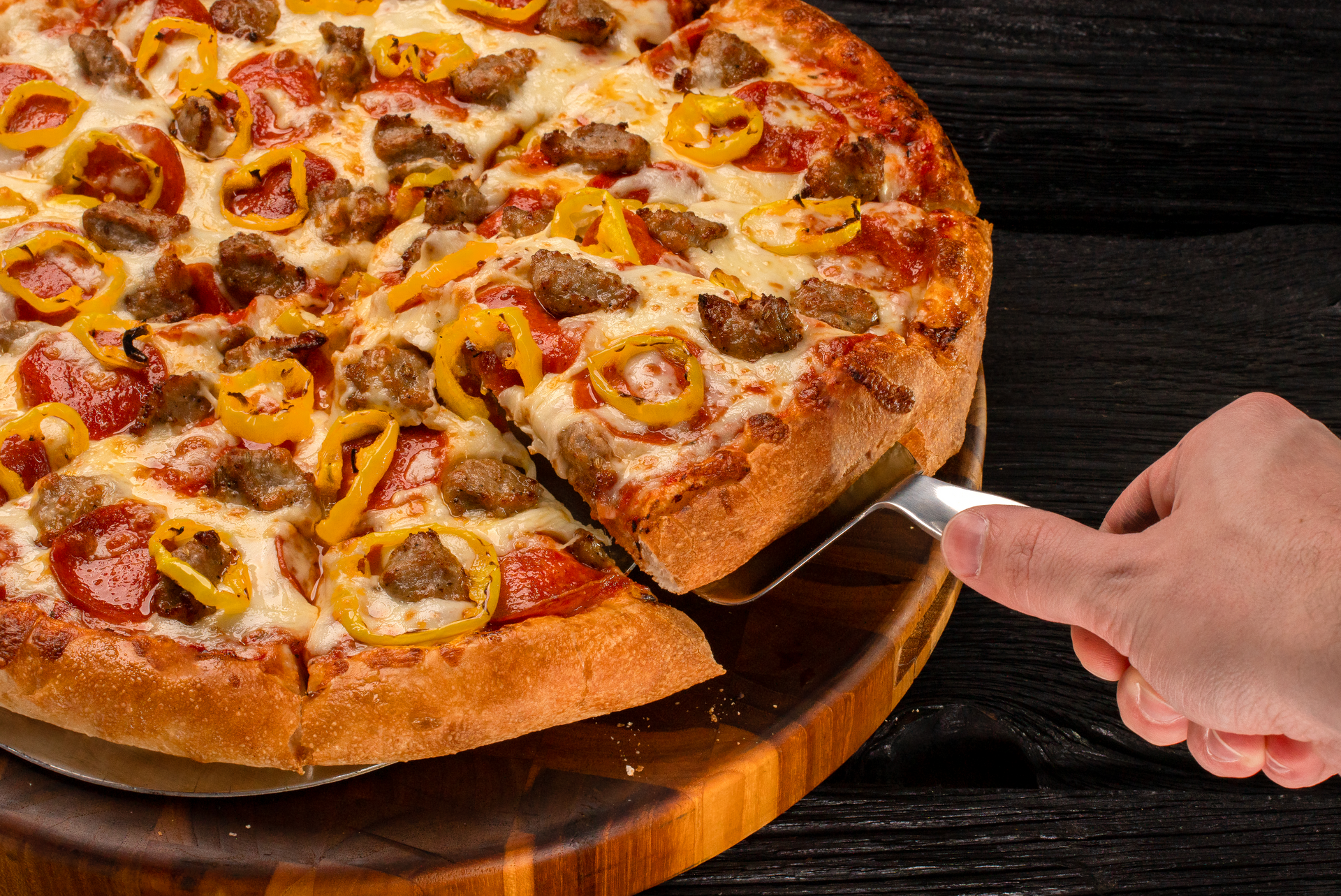 A person taking a slice of loaded pizza from a wooden cutting board with a spatula