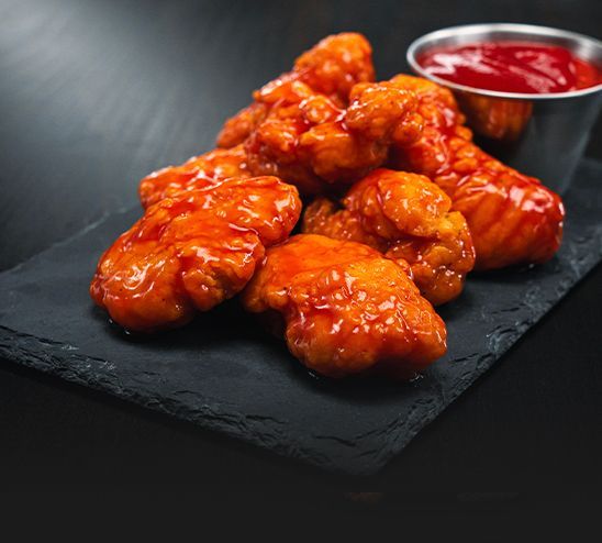 A close up of a plate of chicken wings with red sauce on a table.