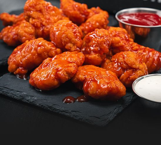 A close up of a plate of chicken wings with bbq sauce and ranch dressing.