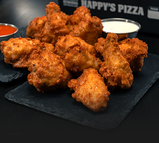 A pile of fried chicken wings on a black plate with dipping sauce.