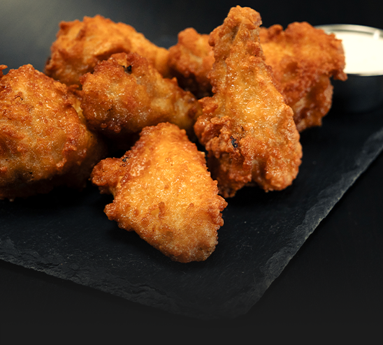 A close up of fried chicken wings on a black plate with dipping sauce.