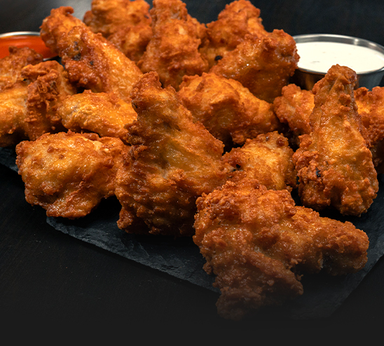 A plate of fried chicken wings with dipping sauce on a table.