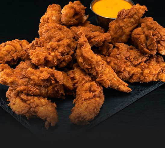A plate of fried chicken with a side of dipping sauce.