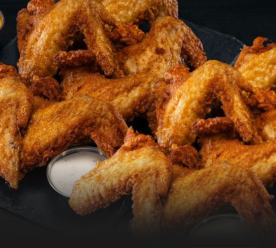 A plate of fried chicken wings with ranch dressing on a table.