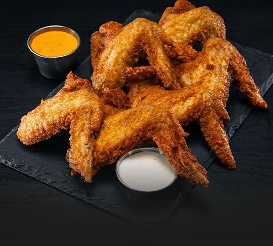 A pile of fried chicken wings with a side of dipping sauce