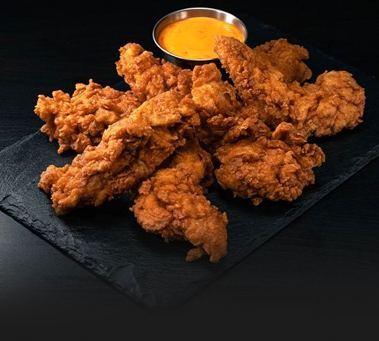 A plate of fried chicken with a dipping sauce on a table.