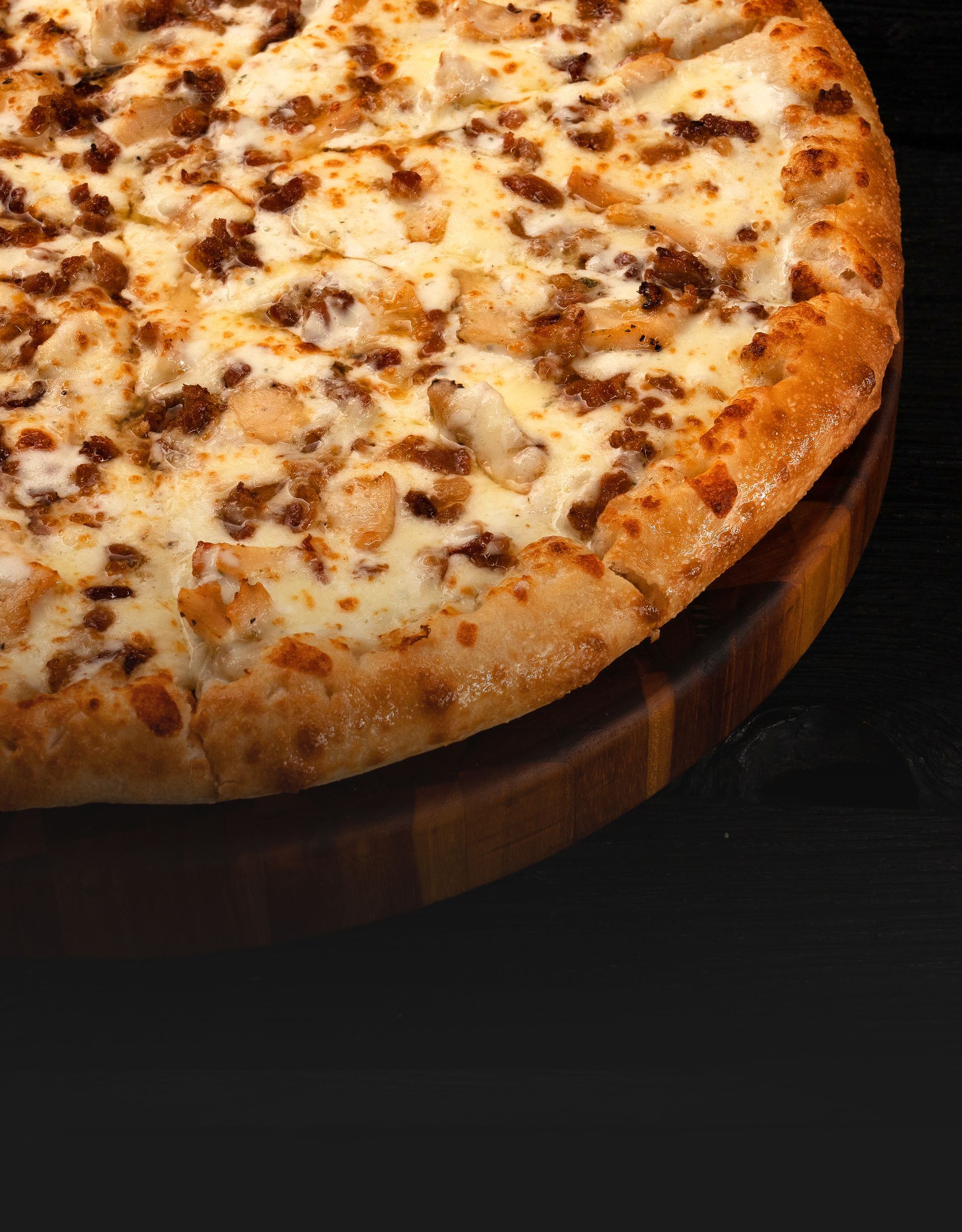 Chicken bacon ranch pizza topped with creamy ranch sauce and melted cheese on a wooden cutting board