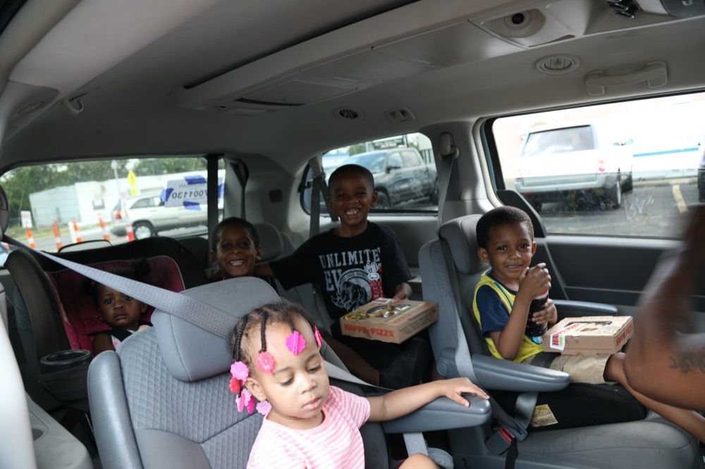 A group of children are sitting in the back seat of a van eating pizza