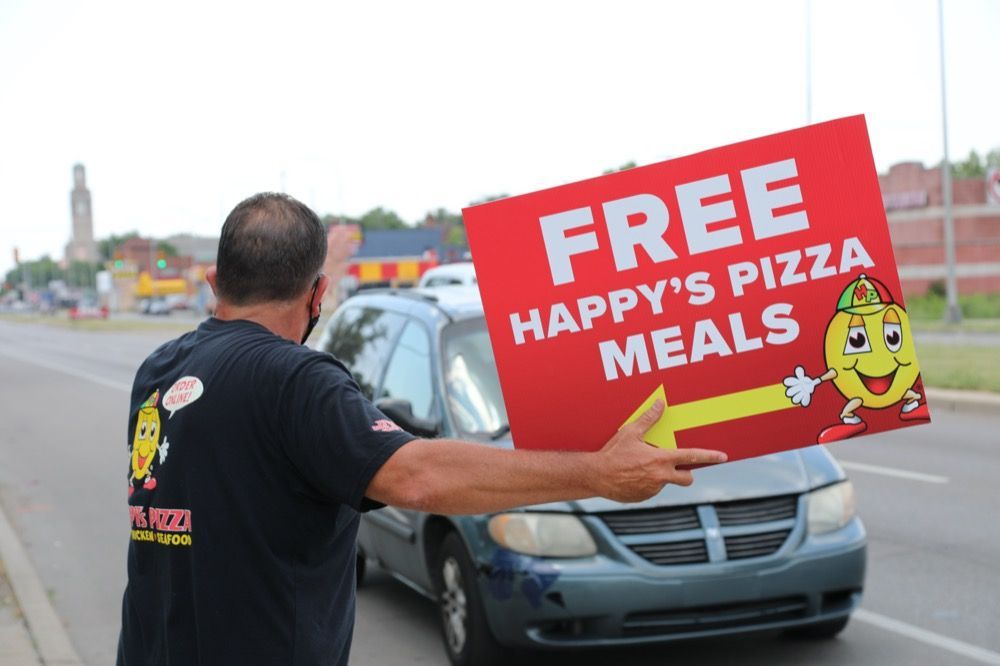 A man is holding a sign that says free happy 's pizza meals