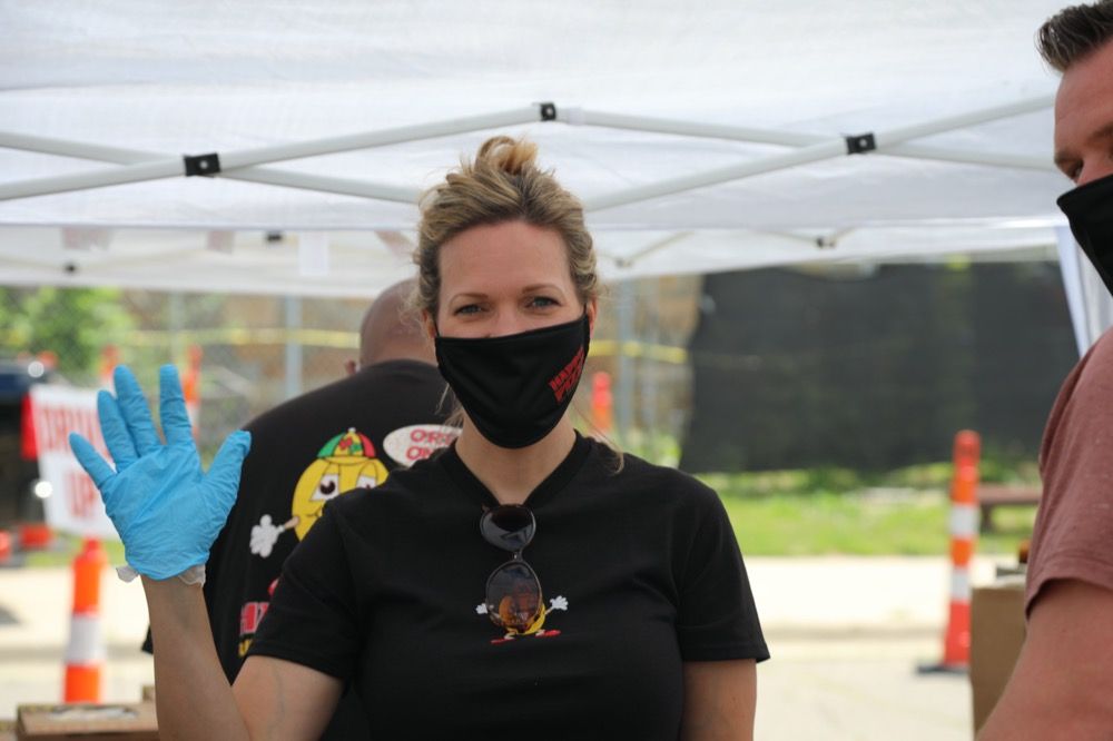 A woman wearing a mask and blue gloves is standing under a tent.