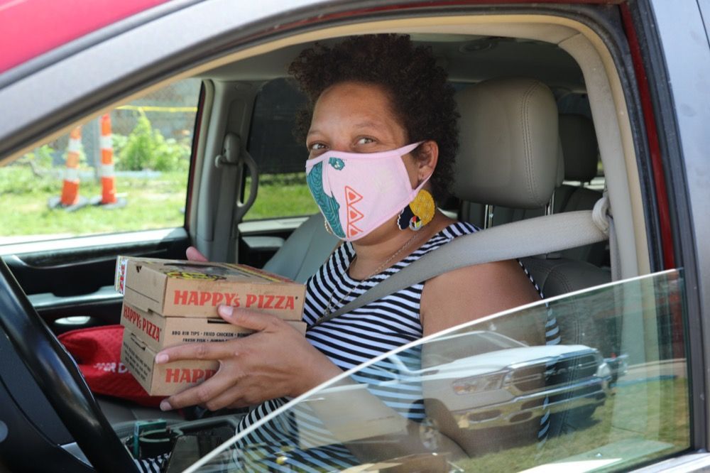 A woman wearing a mask is sitting in a car holding a box of pizza.