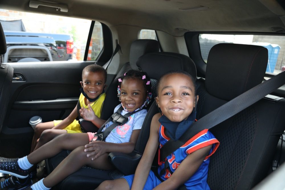 Three children are sitting in the back seat of a car.