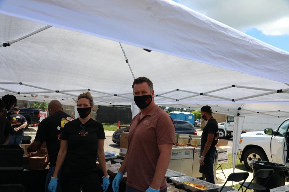 A man and a woman wearing masks and gloves are standing under a tent.