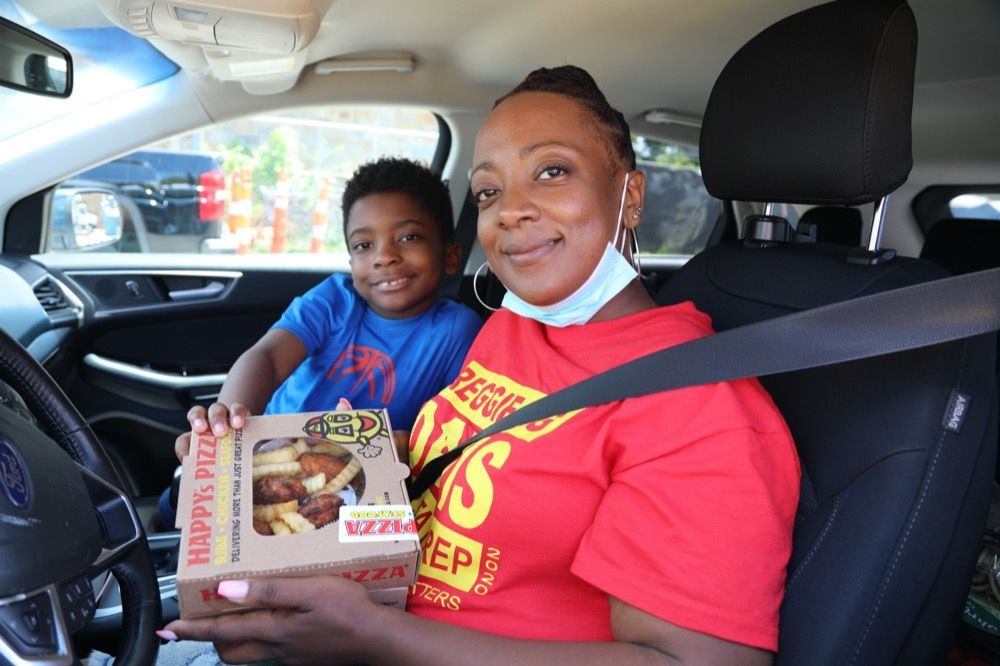 A woman and a boy are sitting in a car holding a box of food.