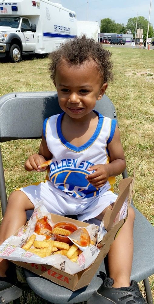 A little boy is sitting in a chair eating a pizza and french fries.