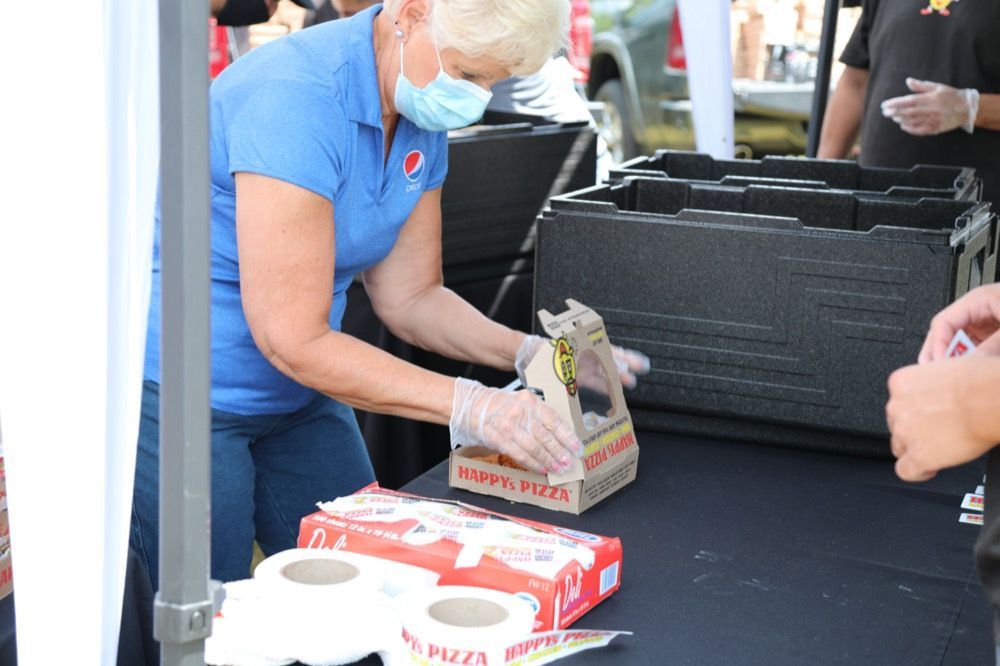 A woman wearing a mask is packing pizza boxes on a table.