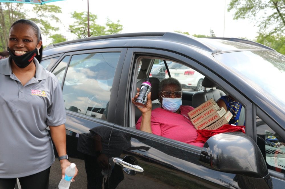 A woman wearing a mask is standing next to a woman in a car.