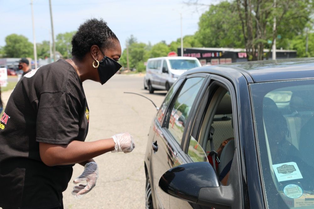 A woman wearing a mask and gloves is standing next to a car.