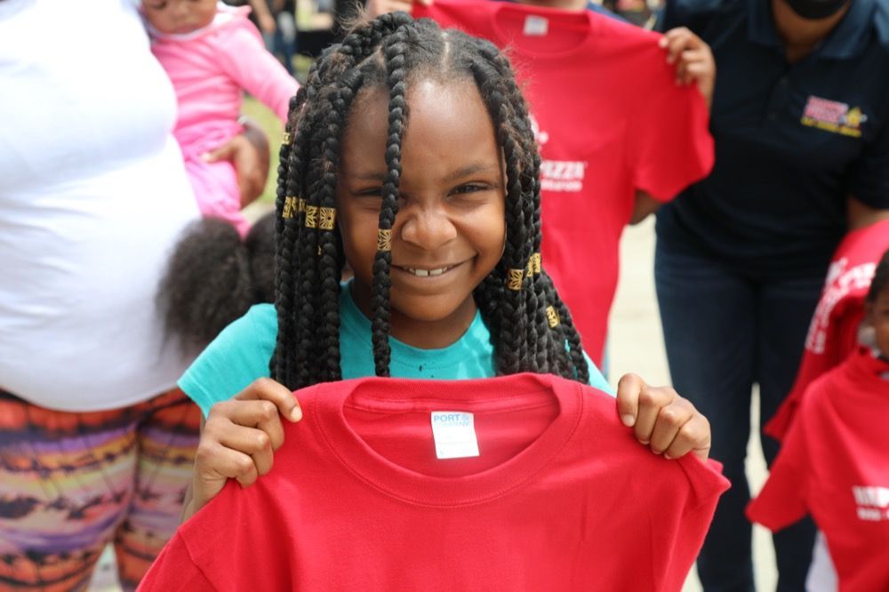 A little girl is holding a red t-shirt with the number 29 on it