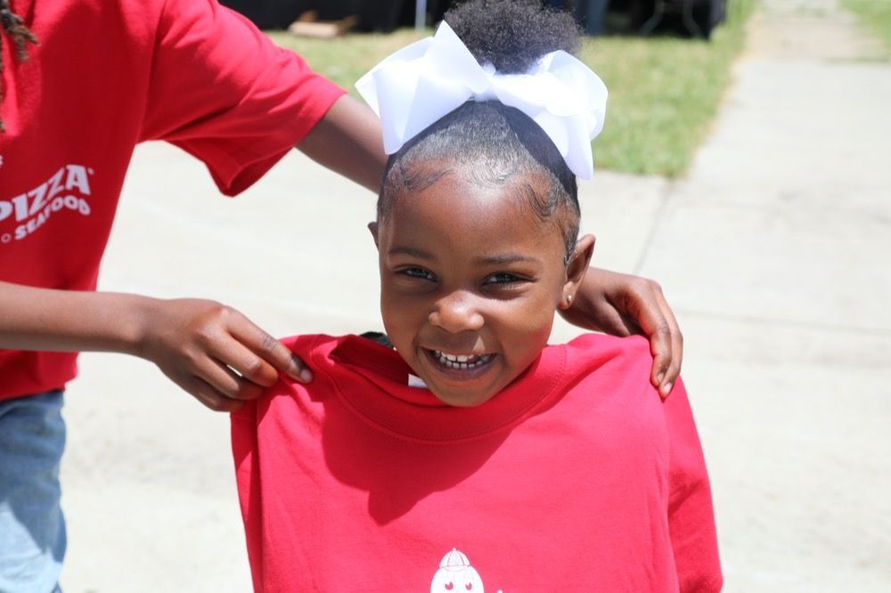 A little girl wearing a red shirt that says pizza on it