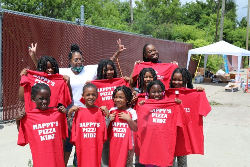 A group of children are holding up red shirts that say happy 's pizza kidz.