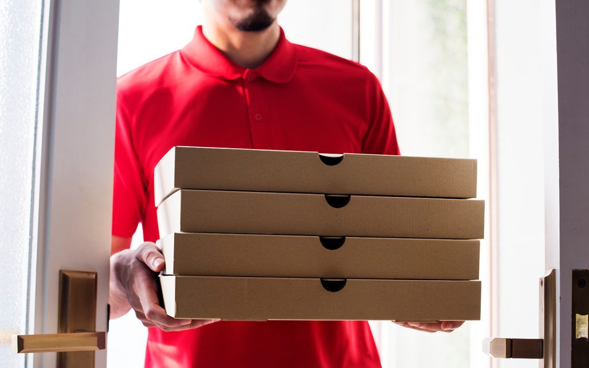 A delivery man in a red shirt is holding a stack of pizza boxes.