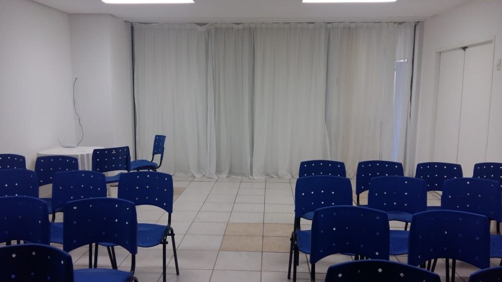 Uma fileira de cadeiras azuis em uma sala com cortinas brancas.