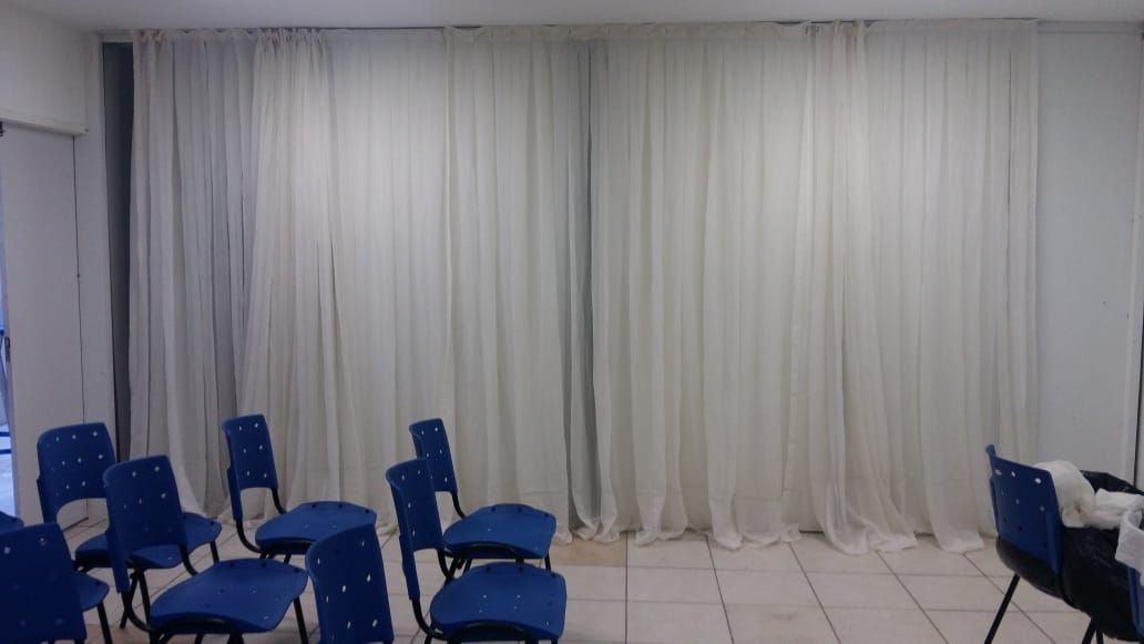 Uma sala de aula com cadeiras azuis e cortinas brancas.