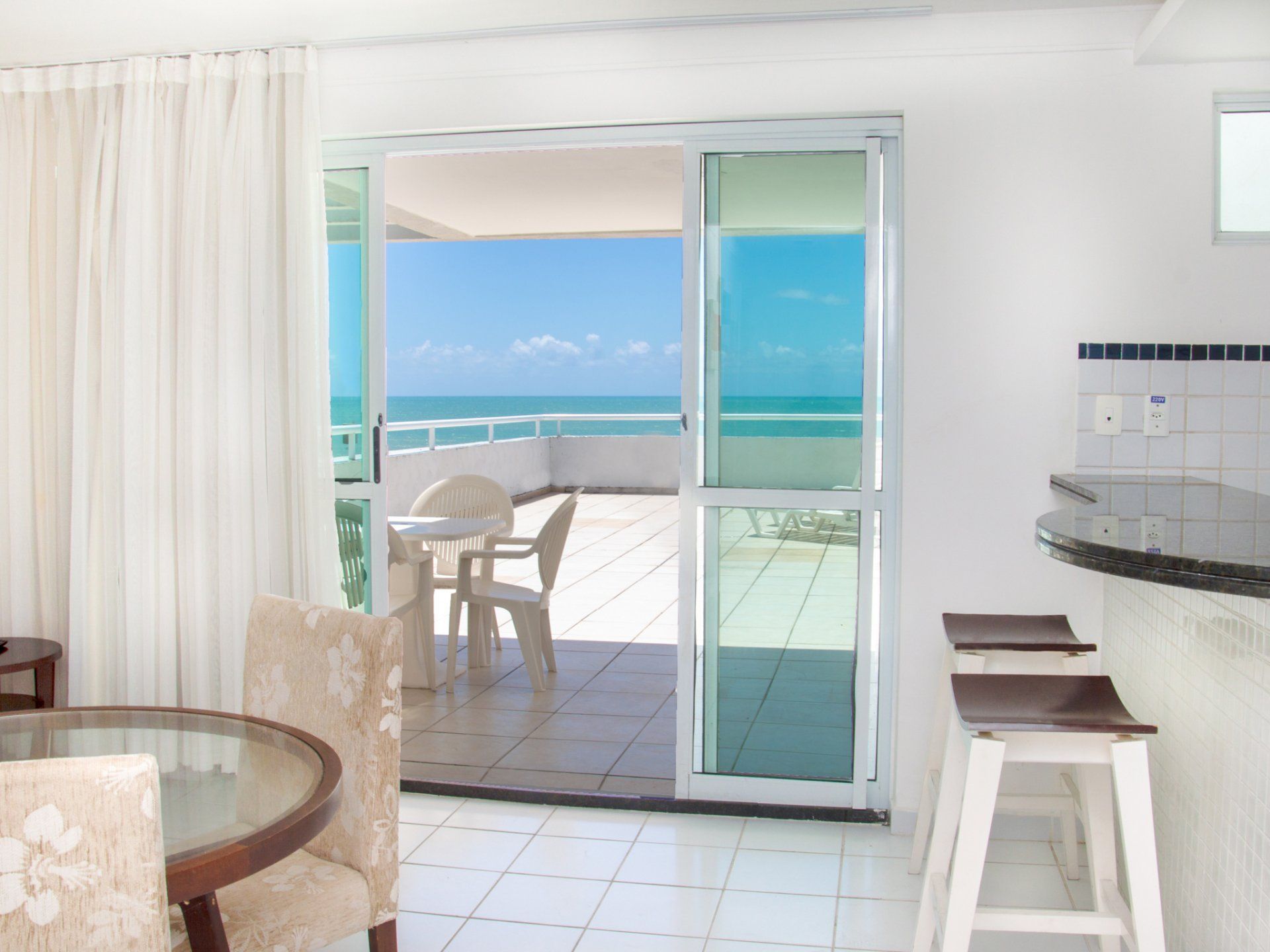 Uma sala de estar com uma porta de vidro deslizante que leva a uma varanda com vista para o oceano