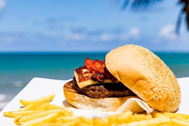 Um hambúrguer e batatas fritas em um prato branco na praia.