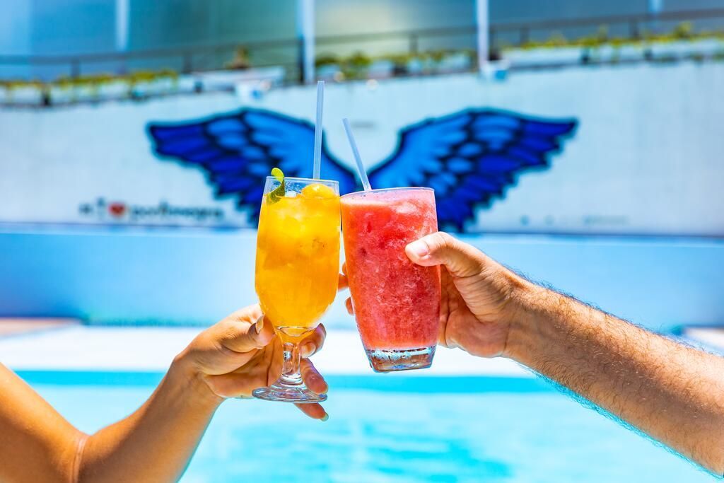 Um homem e uma mulher estão brindando com bebidas em frente a uma piscina.