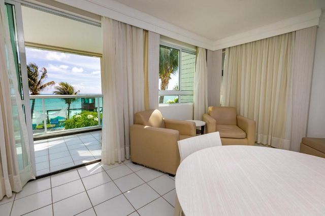 Uma sala de estar com mesa e cadeiras e uma varanda com vista para o oceano.