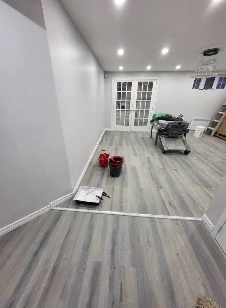 Un sous-sol avec parquet imitation bois gris, murs blancs et éclairage encastré. Des portes-fenêtres donnent sur l'extérieur.