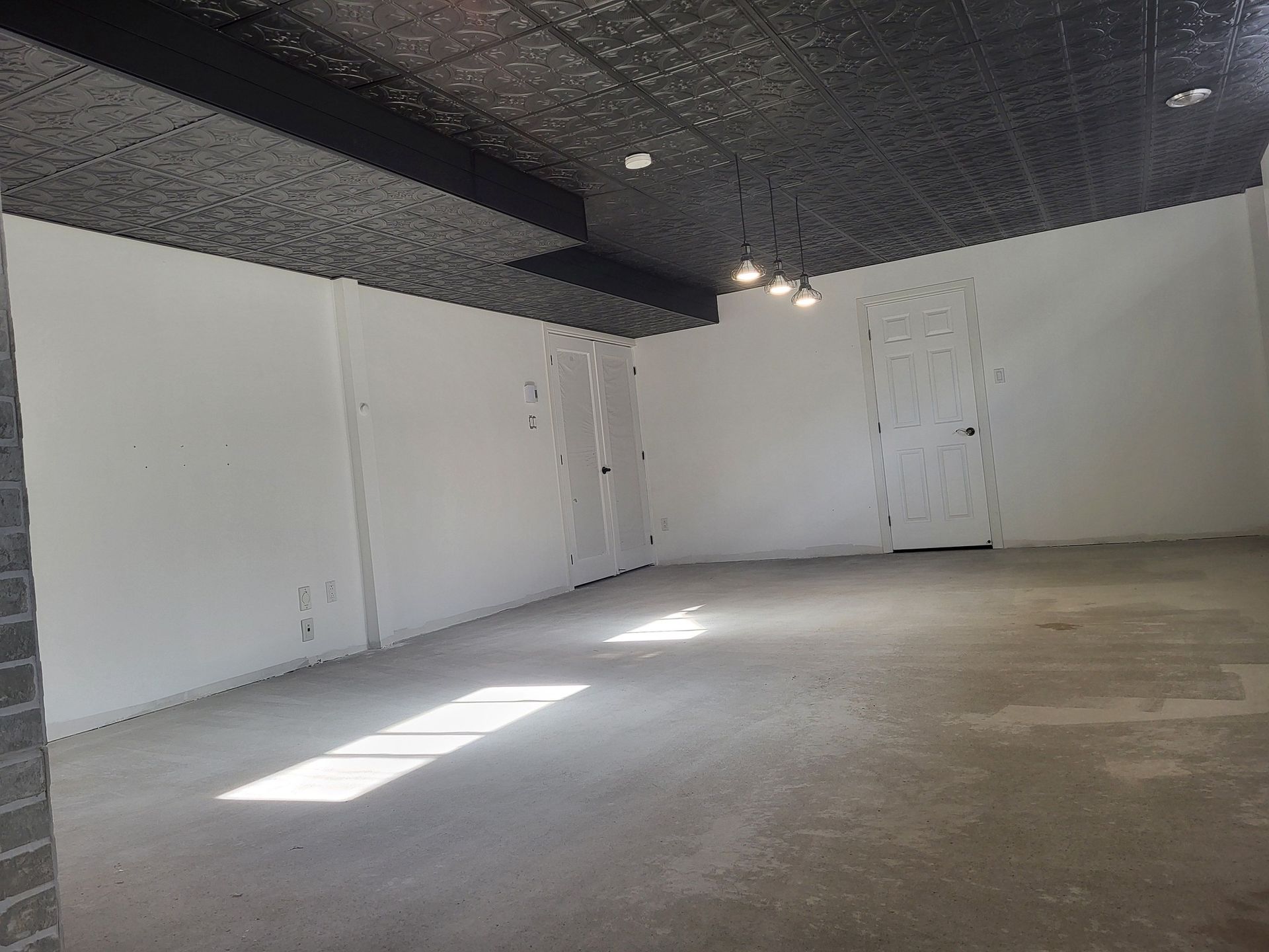 Espace intérieur vide avec des murs blancs et un plafond texturé sombre ; la lumière du soleil traverse le sol en béton.