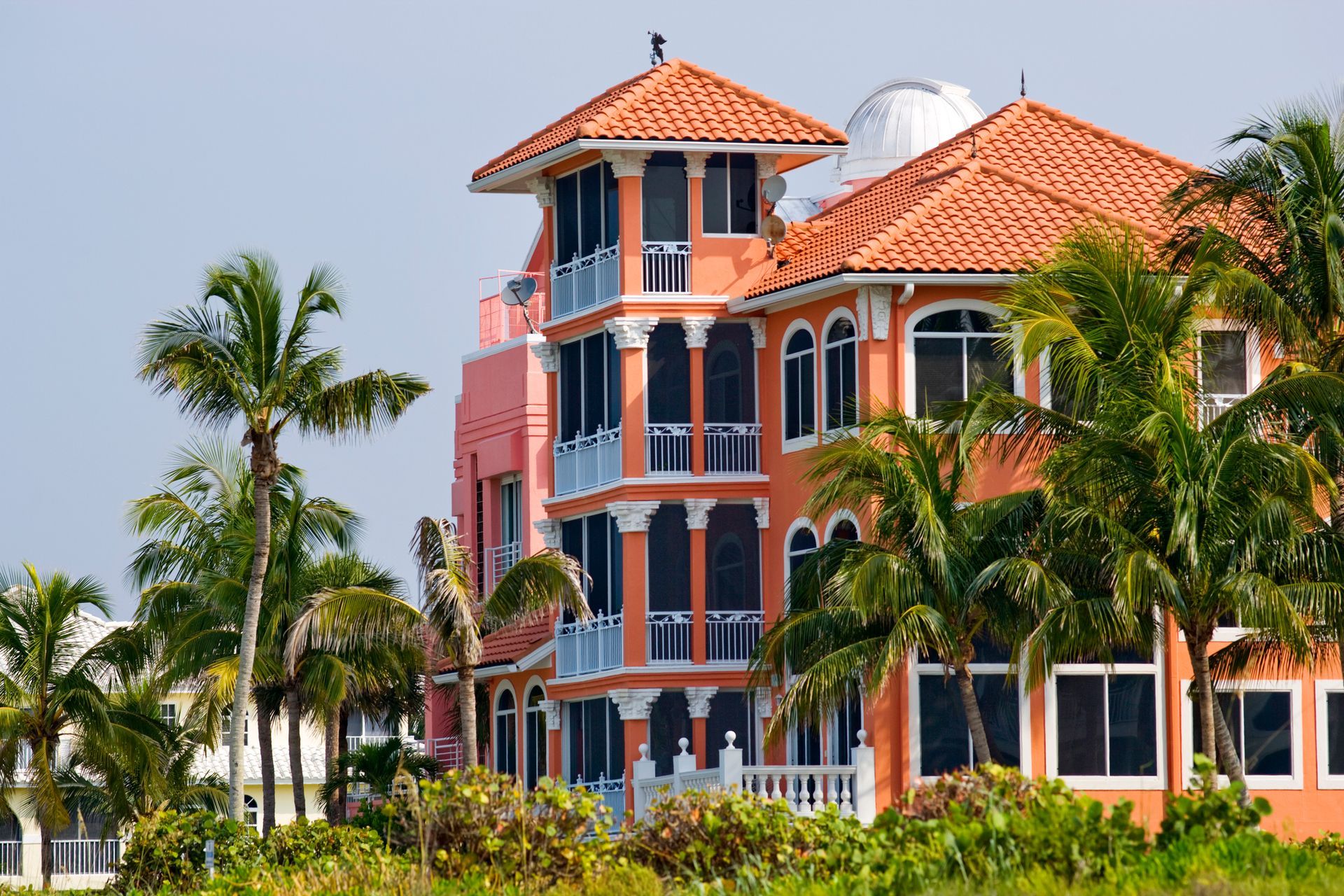 A large orange building with a tiled roof is surrounded by palm trees.