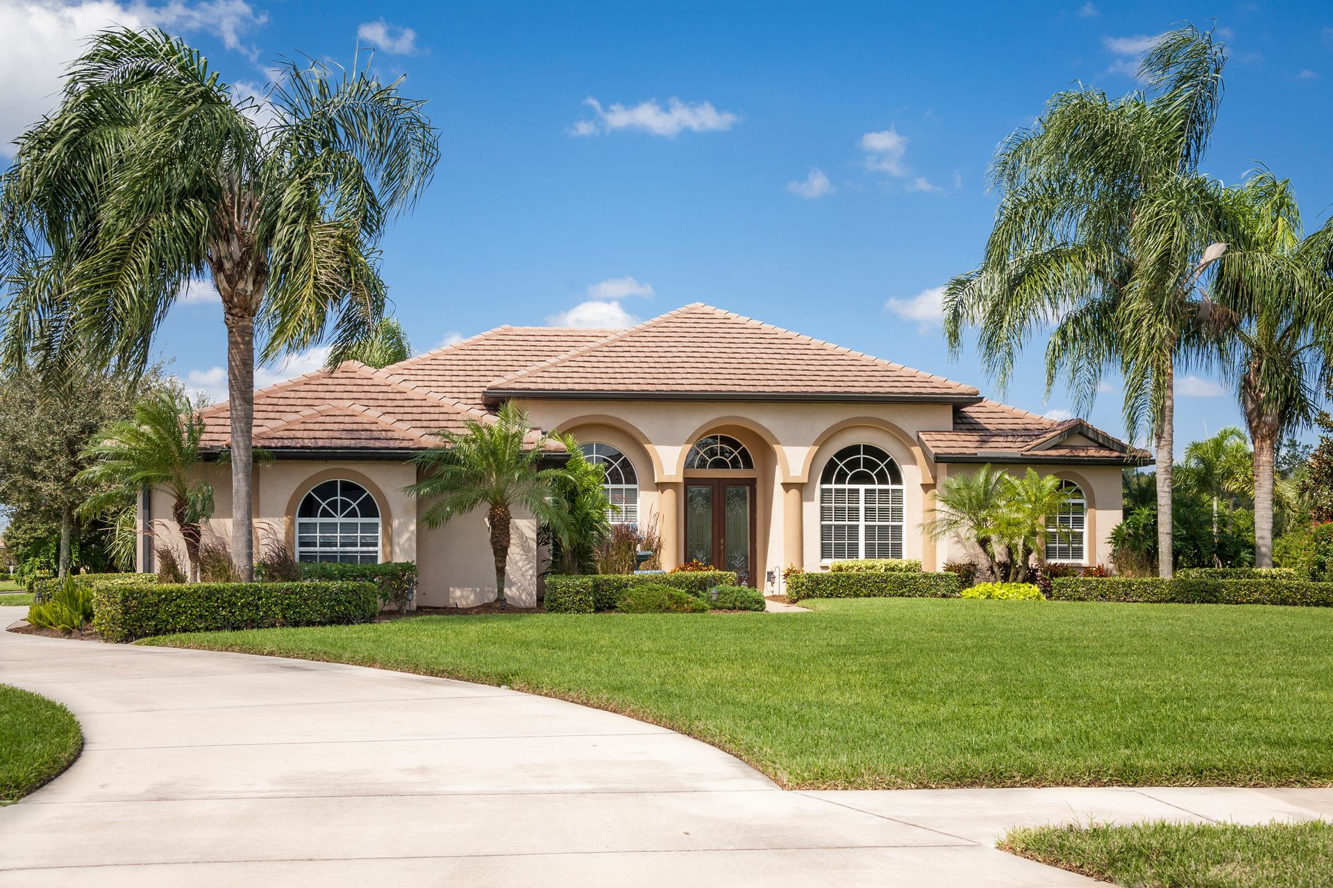 A large house with a driveway and palm trees in front of it.