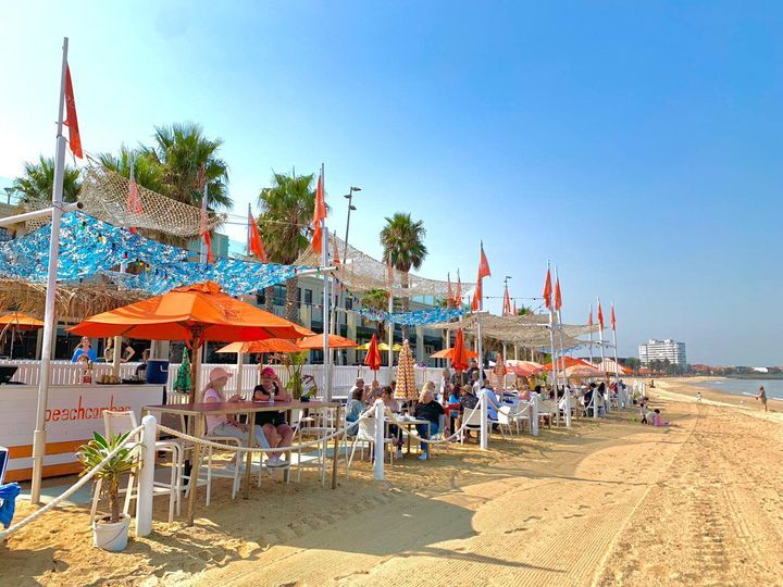 A beach with tables and chairs and umbrellas on a sunny day.