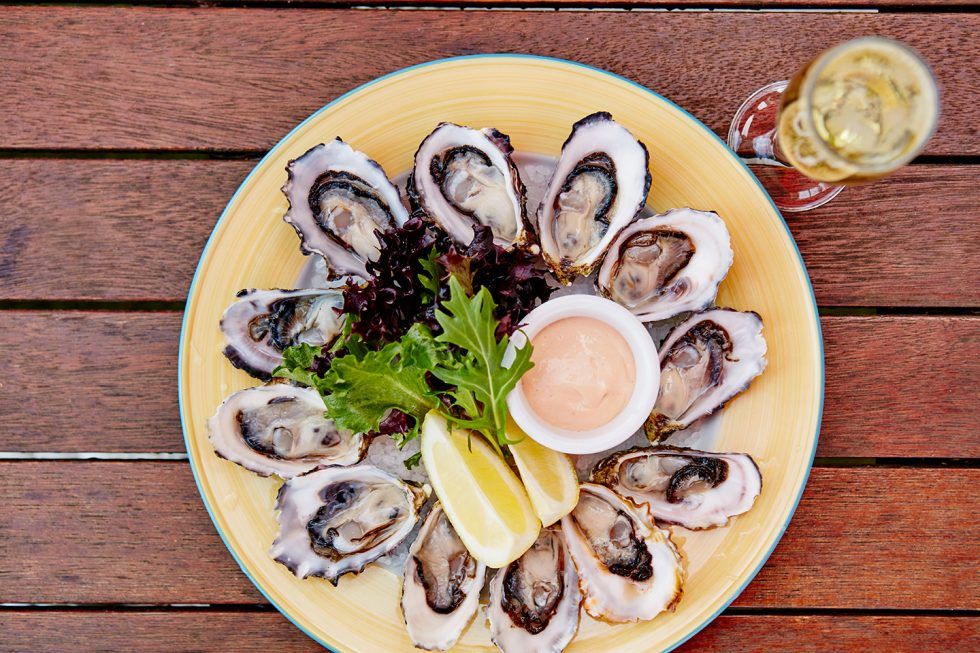 A plate of oysters on a wooden table next to a glass of wine.