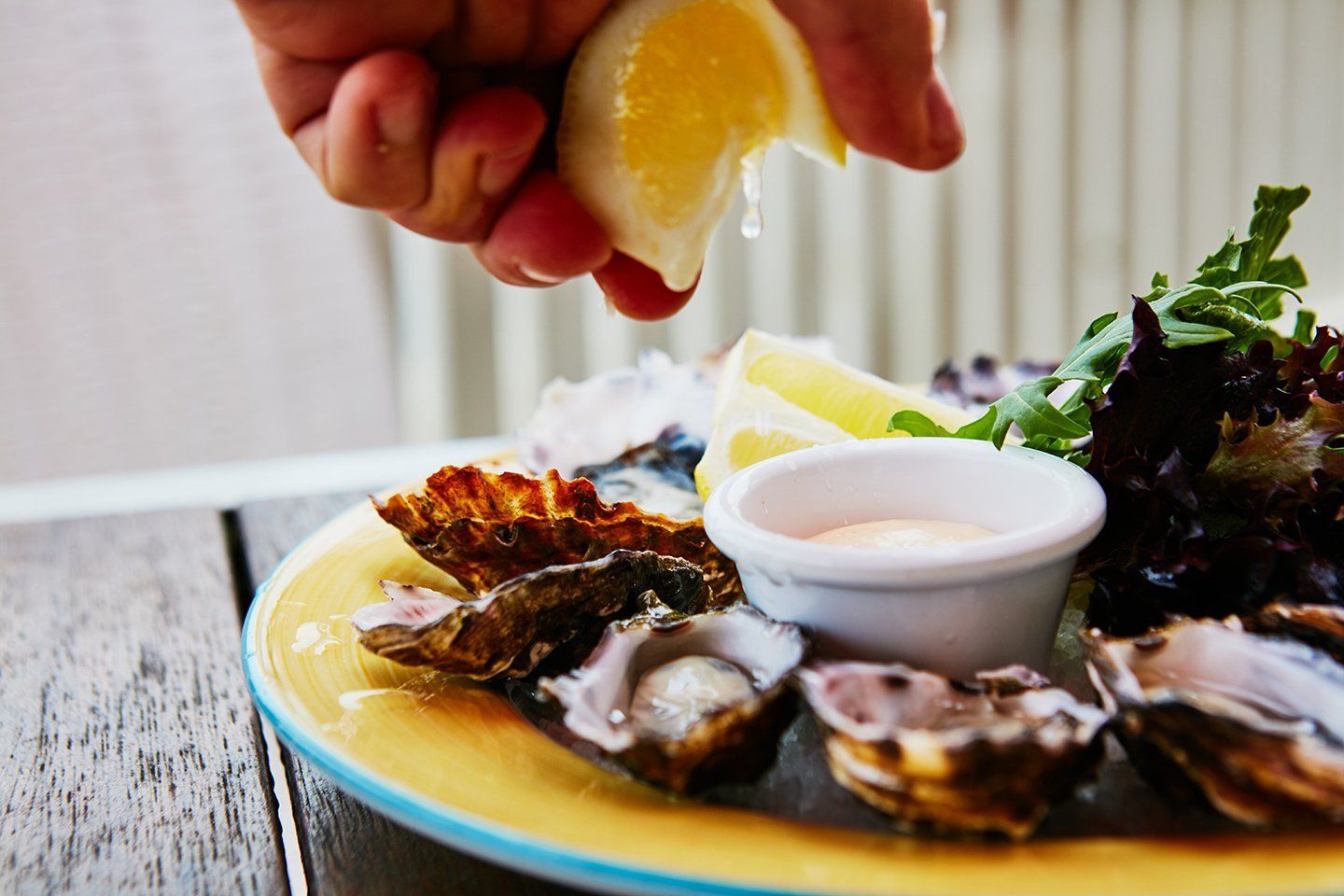 A person is squeezing a lemon over a plate of oysters.