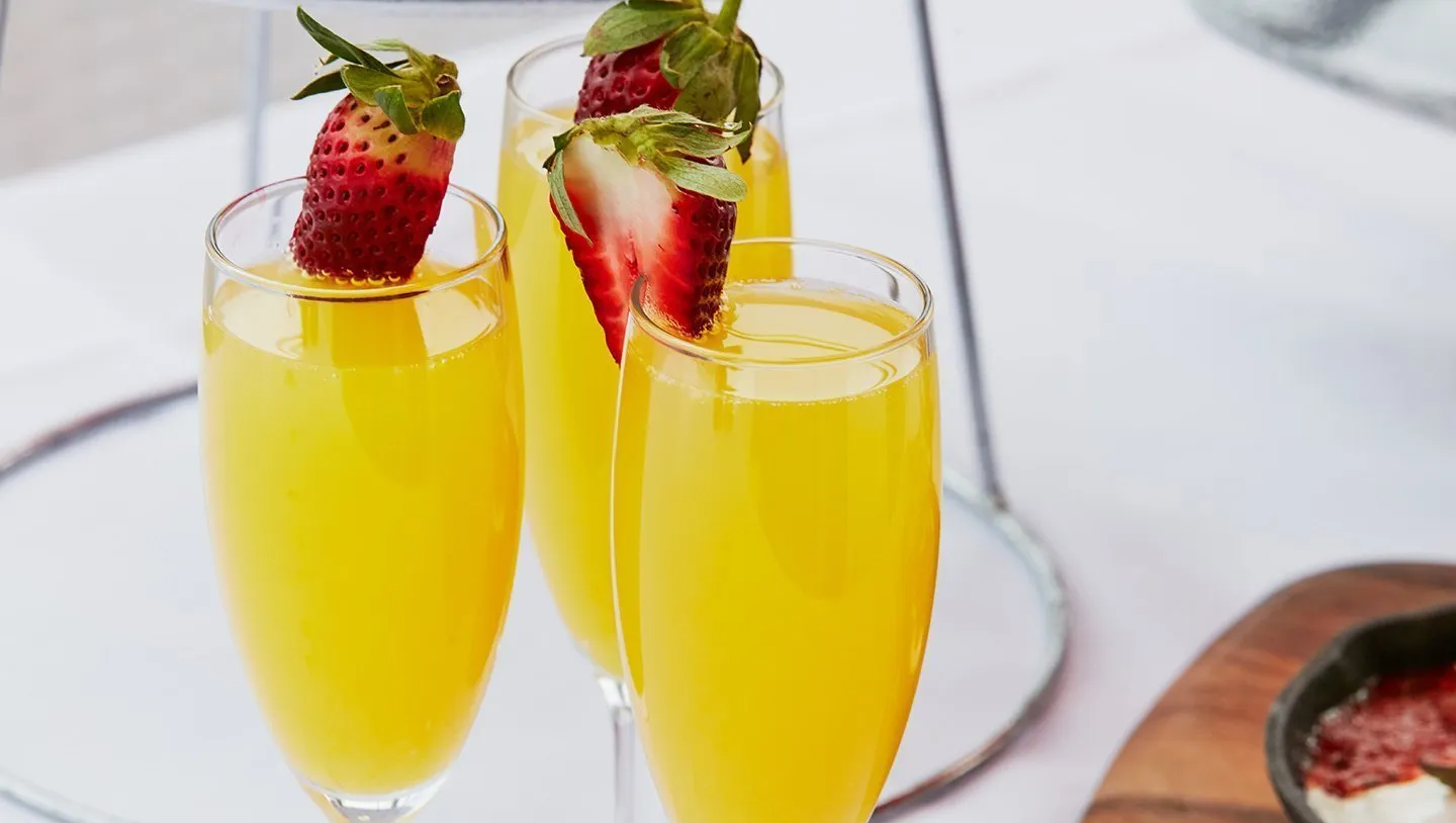 Three glasses of orange juice with strawberries in them on a table.