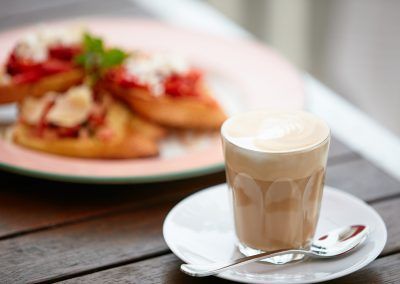 A cup of coffee is on a saucer next to a plate of food.