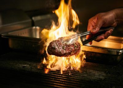 A person is cooking a steak on a grill with flames coming out of it.