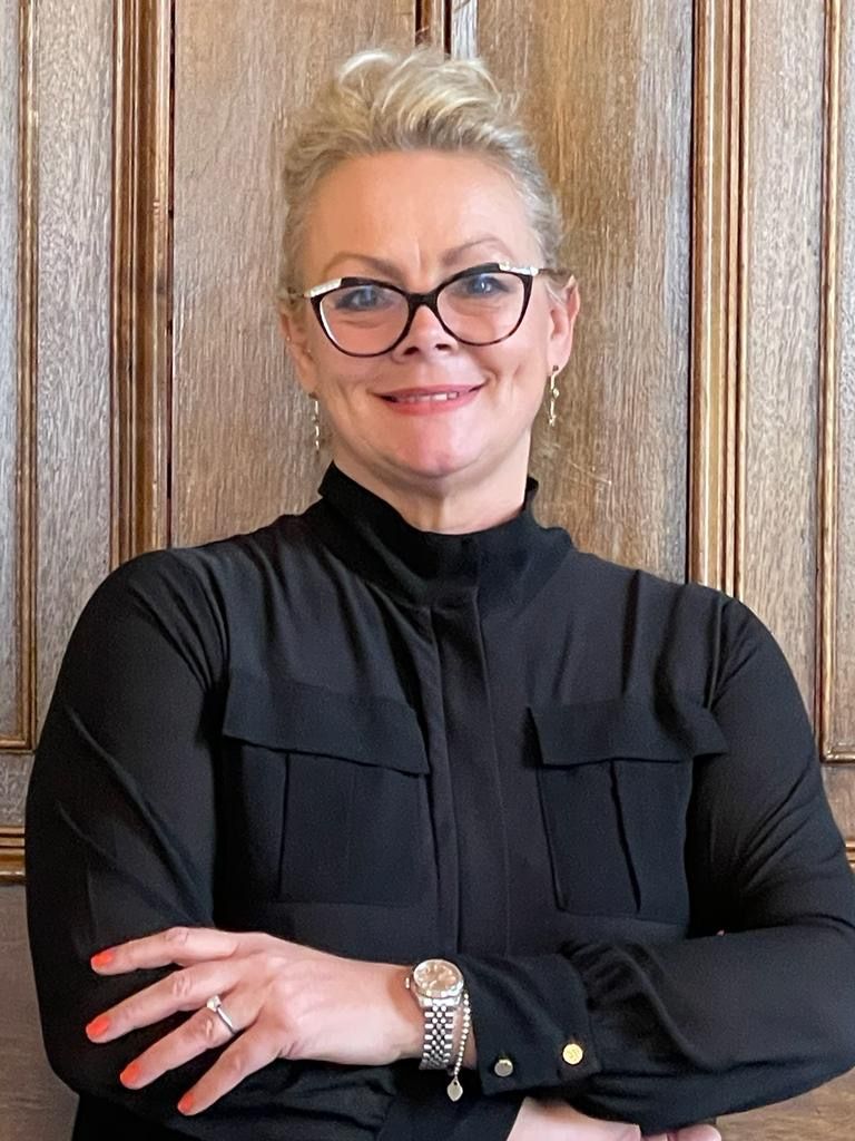 A woman wearing glasses and a black shirt is standing with her arms crossed.